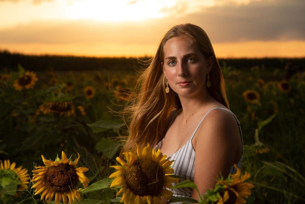High school senior portrait in a Kansas City sunflower field at golden hour, showcasing a fine art senior photography session.